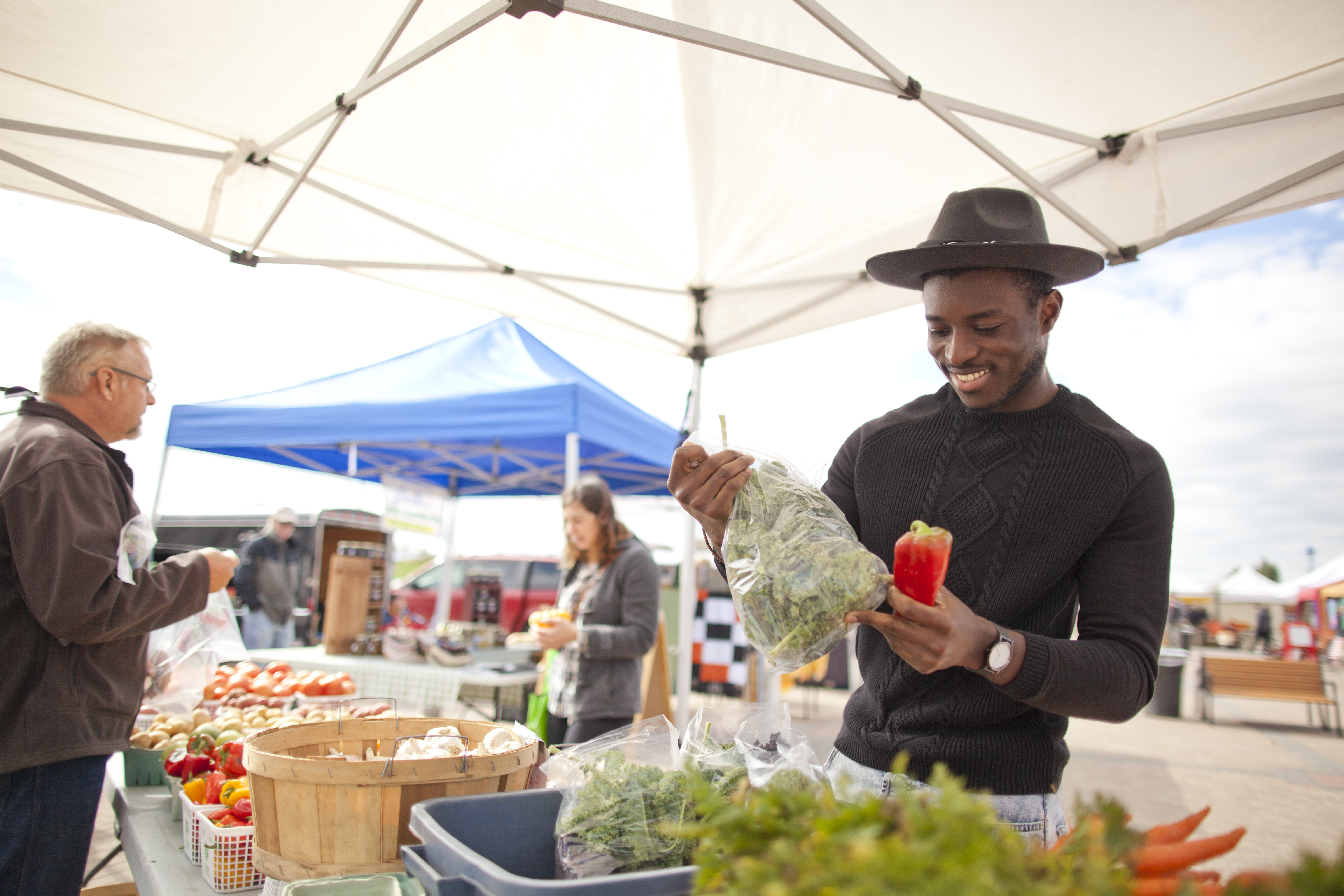 A man in a hat looks at produce at the local Farmers Market